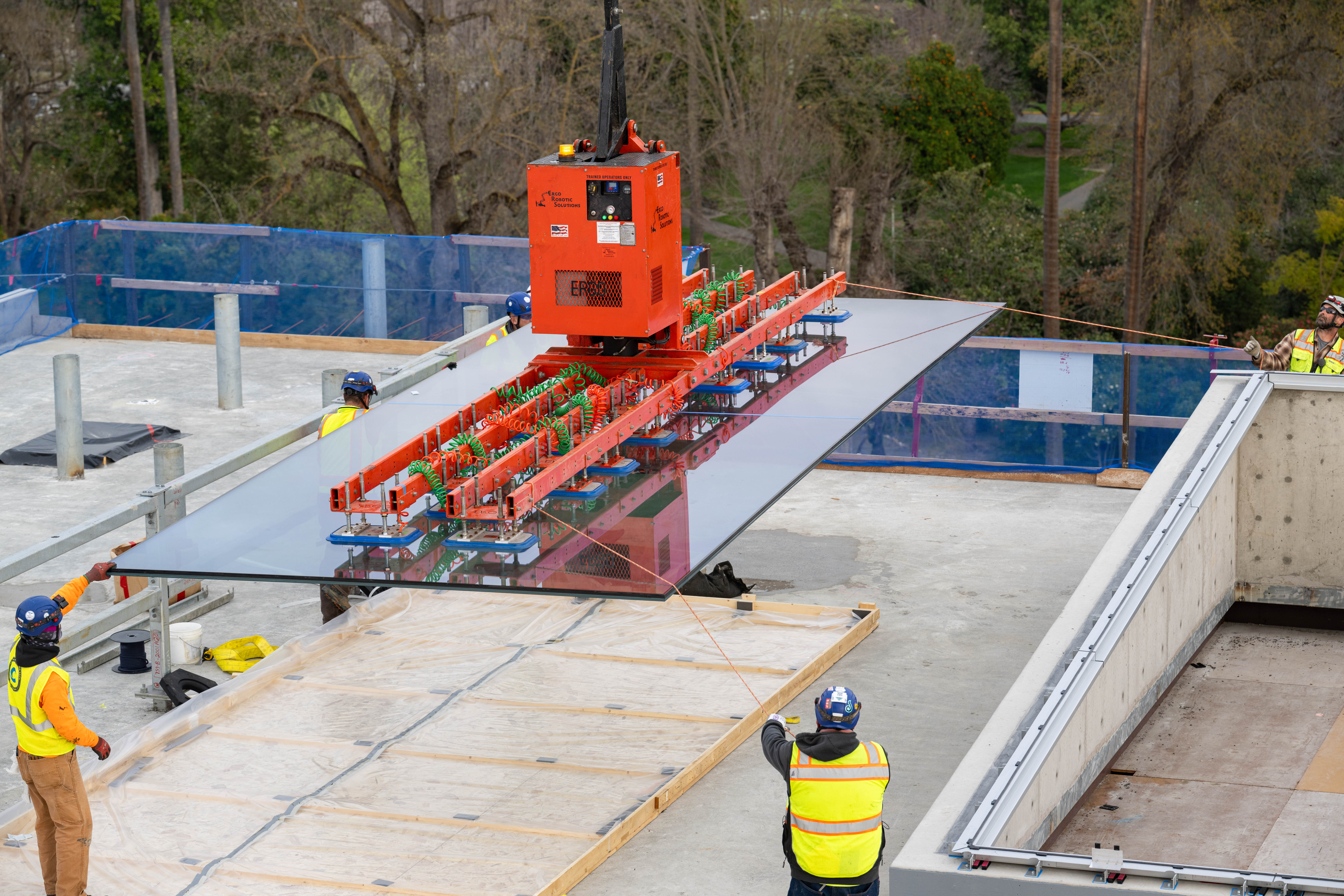 A crew guides a large glass panel into place on the roof.