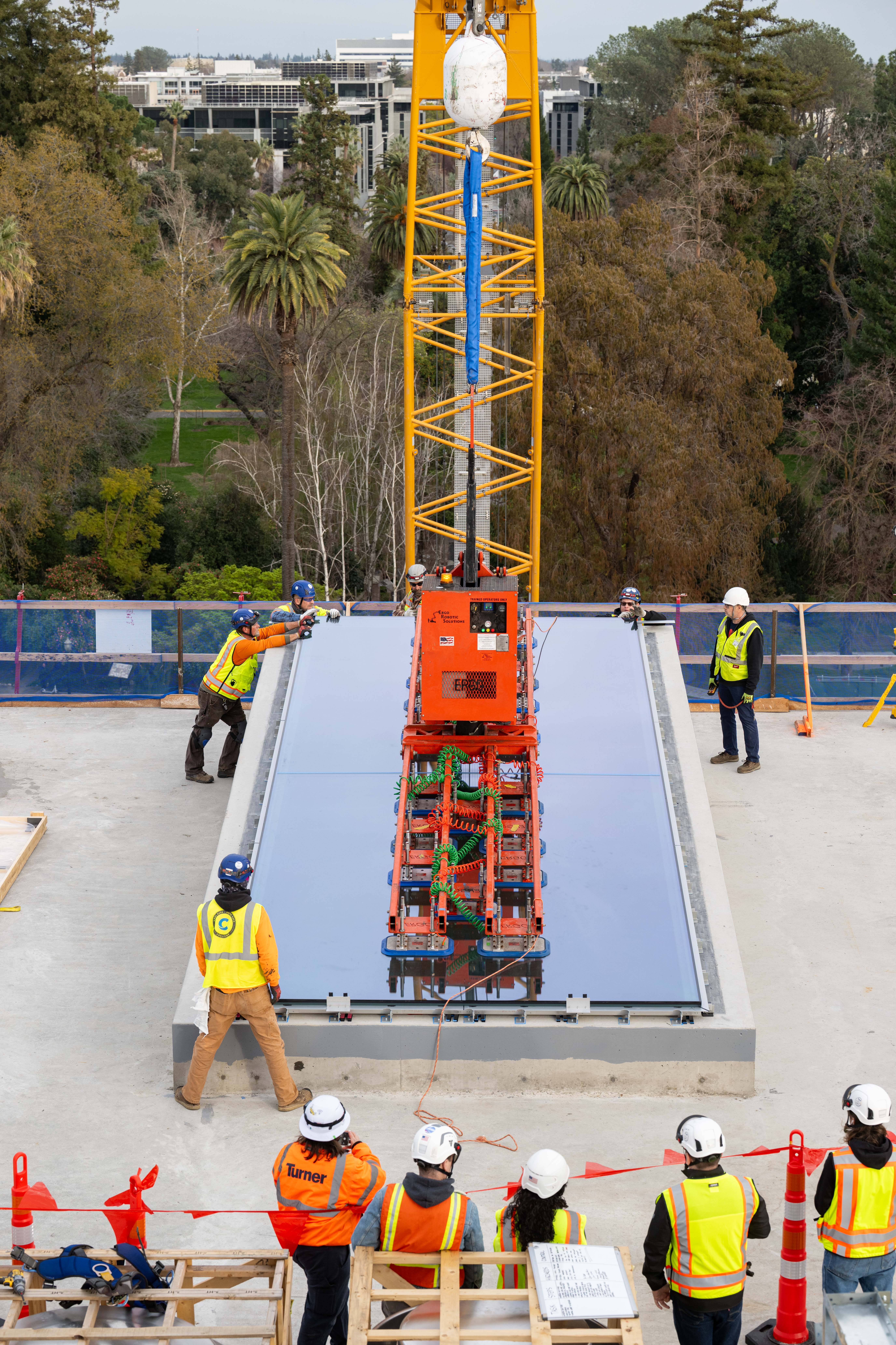 Workers use a vacuum lifter to hoist a large glass sheet.