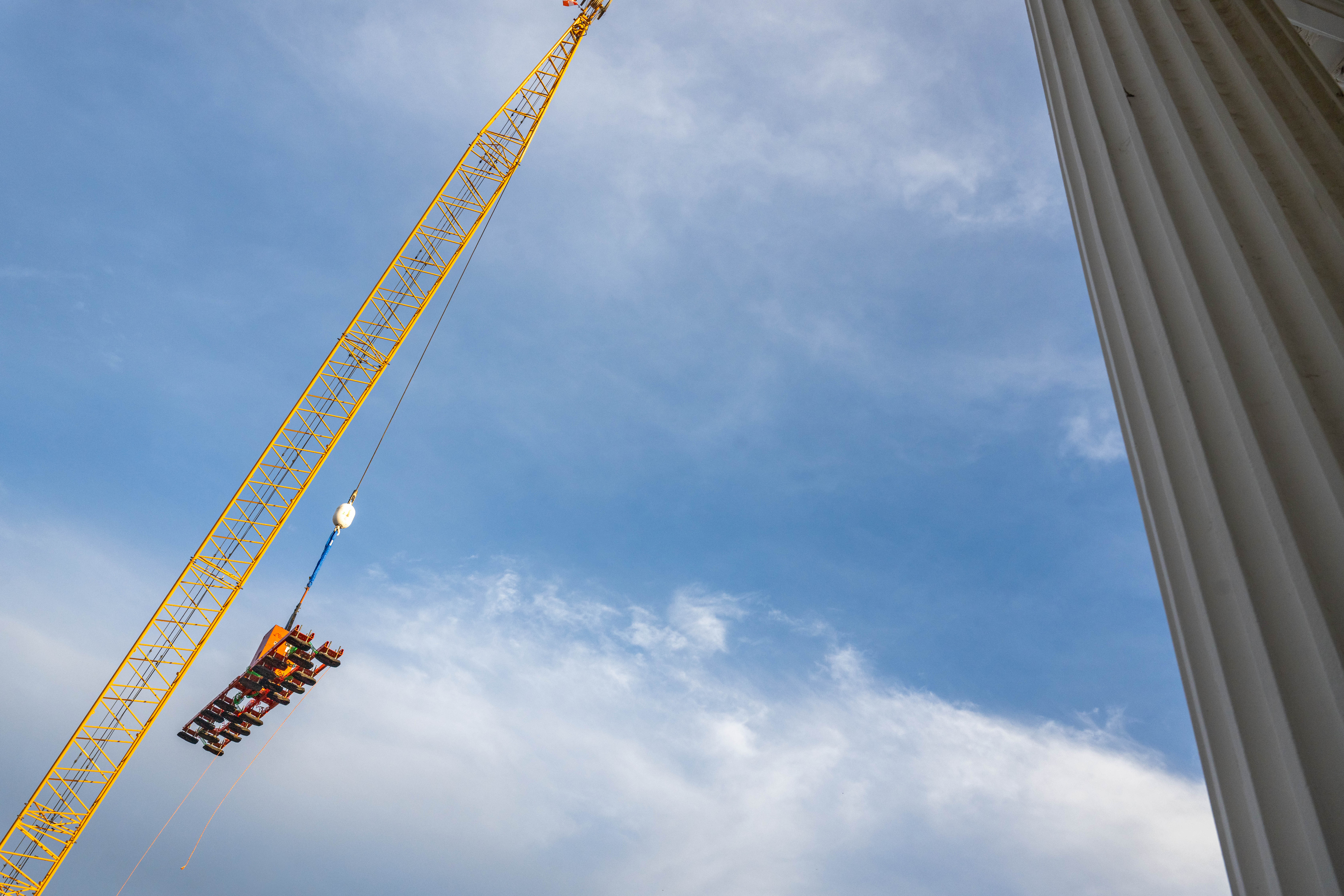A yellow construction crane lifts glass equipment.